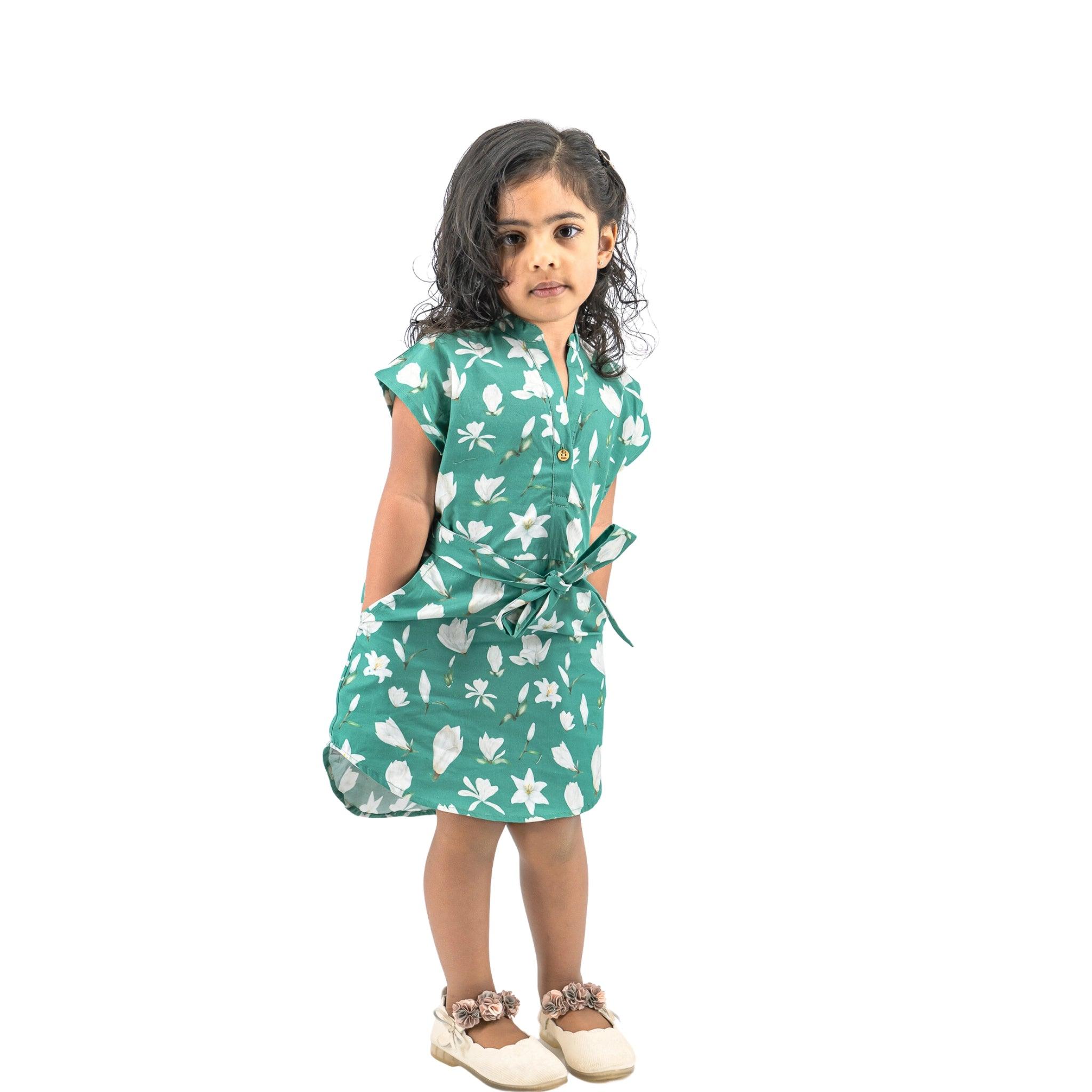 A young girl in a Bottle Green Lilly Blossom Cotton Shirt Dress for Kids by Karee stands looking at the camera, isolated on a white background.