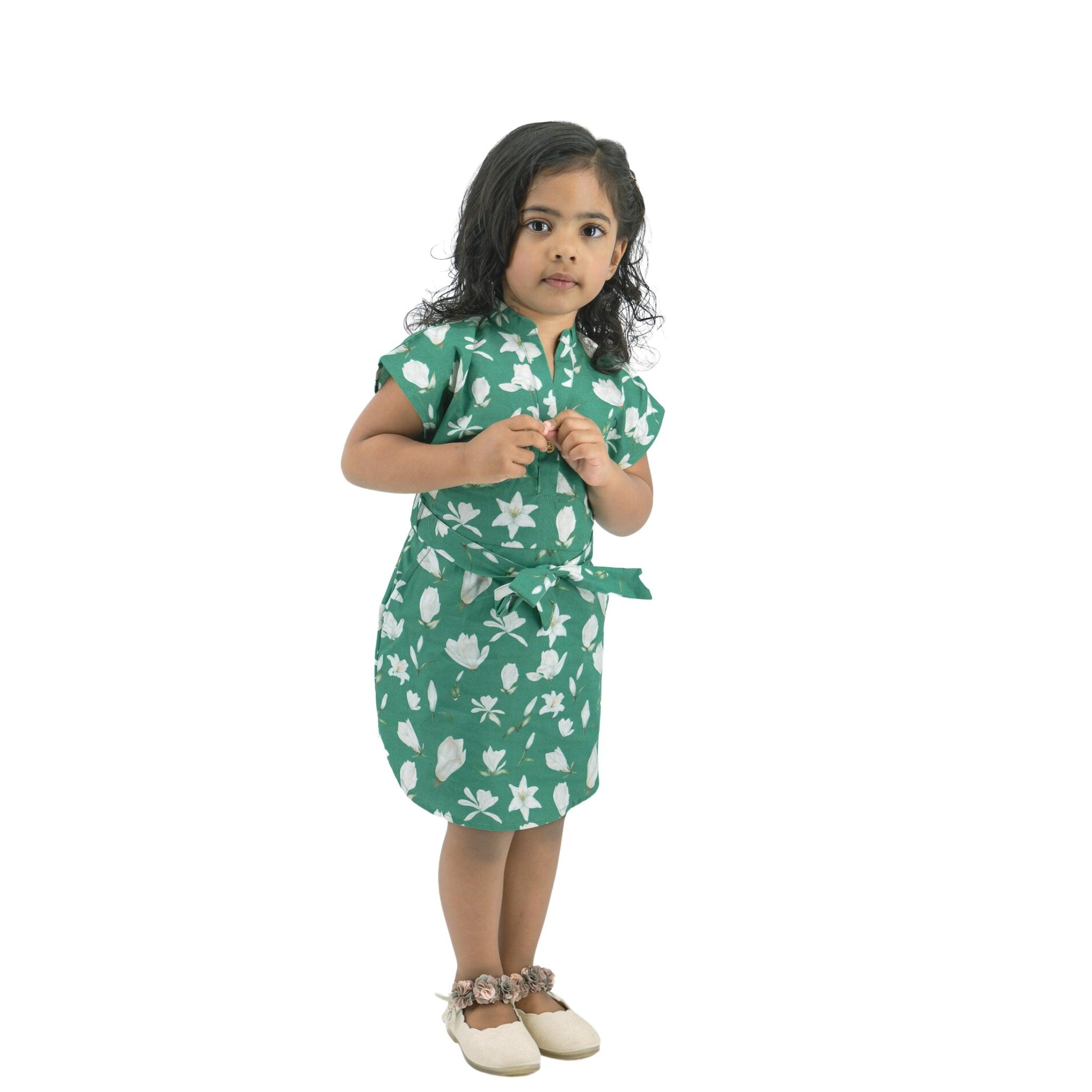 A young girl in a "Bottle Green Lilly Blossom Cotton Shirt Dress for Kids" by Karee and white shoes standing against a white background, looking to the side.