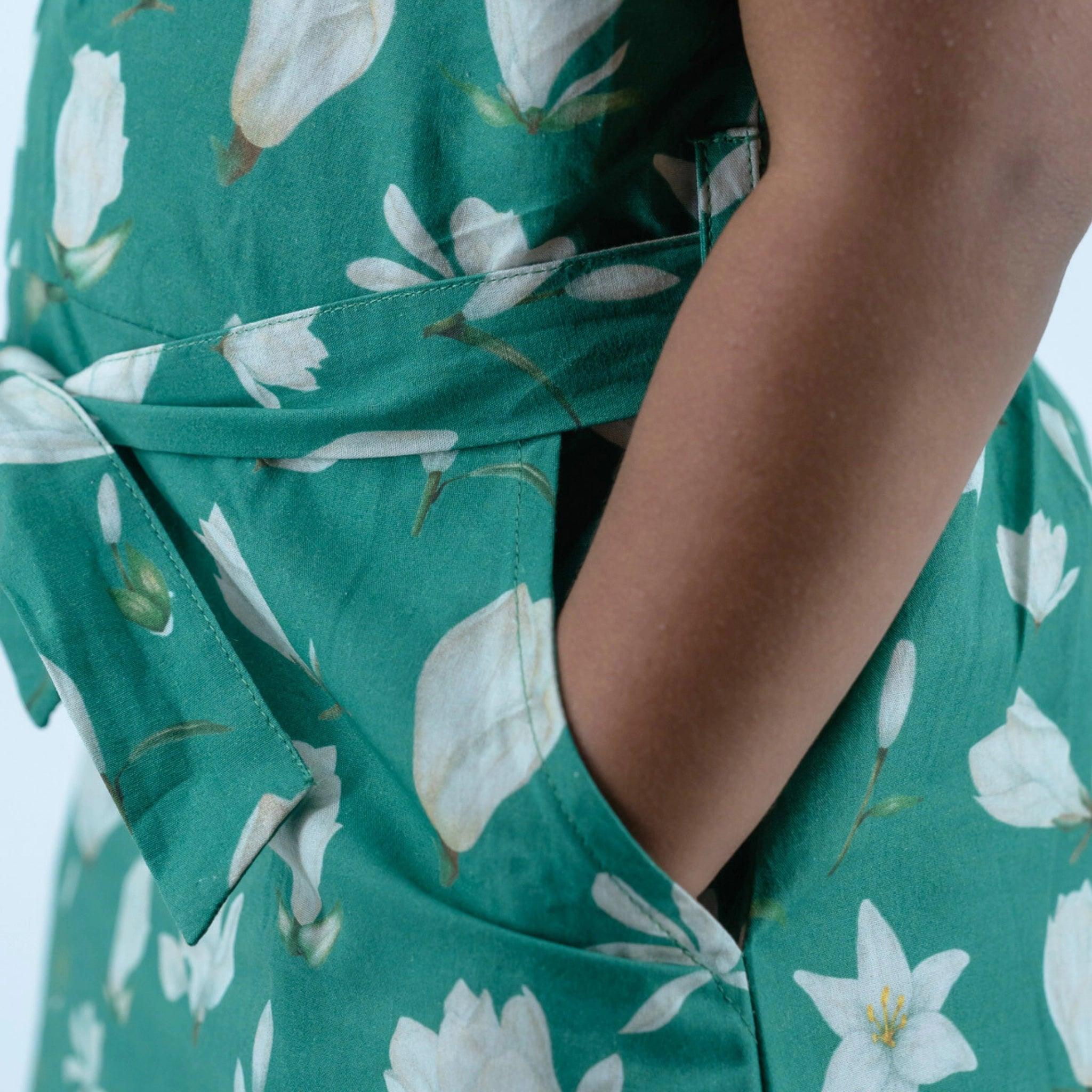 Close-up of a person wearing a Karee Bottle Green Lilly Blossom Cotton Shirt Dress for Kids with a white floral pattern, focusing on the waistline and fabric detail.