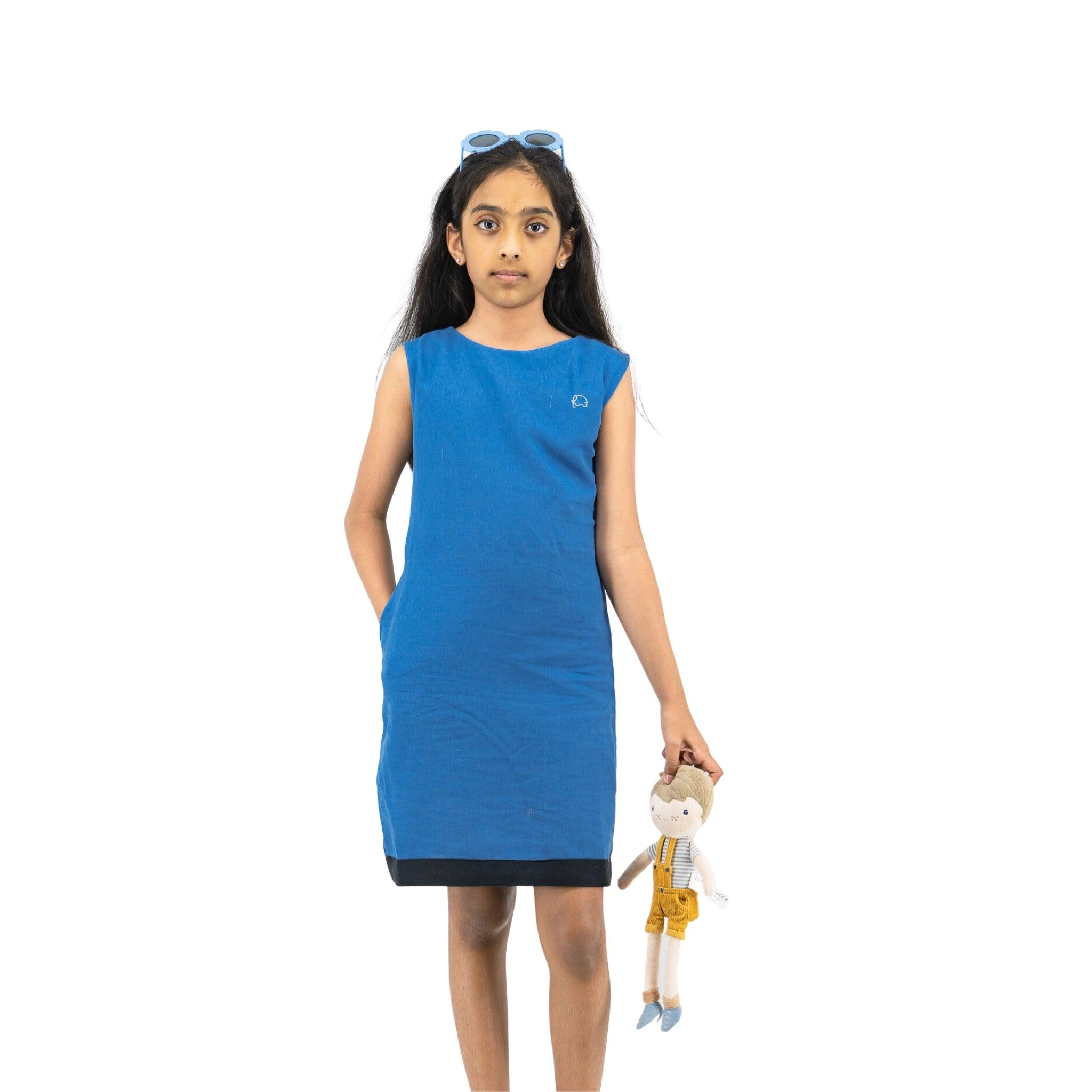 Girl in Karee's Linen Cotton Round Neck Frock for Kids dress with sunglasses on her head, holding a doll, standing against a white background.