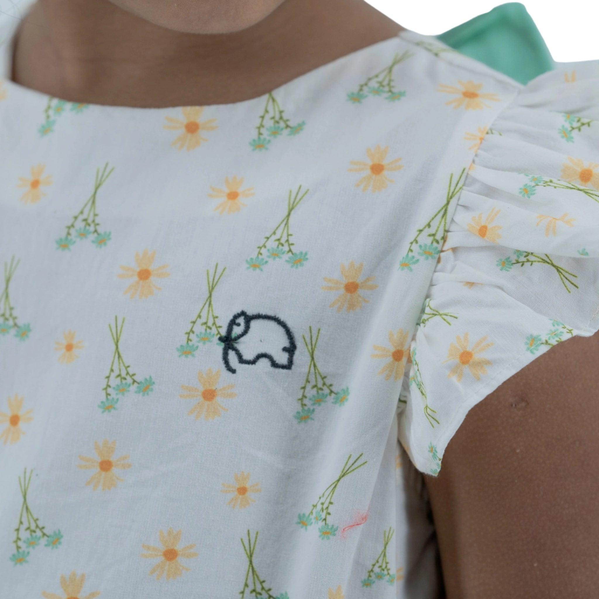 Close-up of a person wearing a Karee Petite Blossom Cotton Dress in Smoked Pearl with a small embroidered car design.
