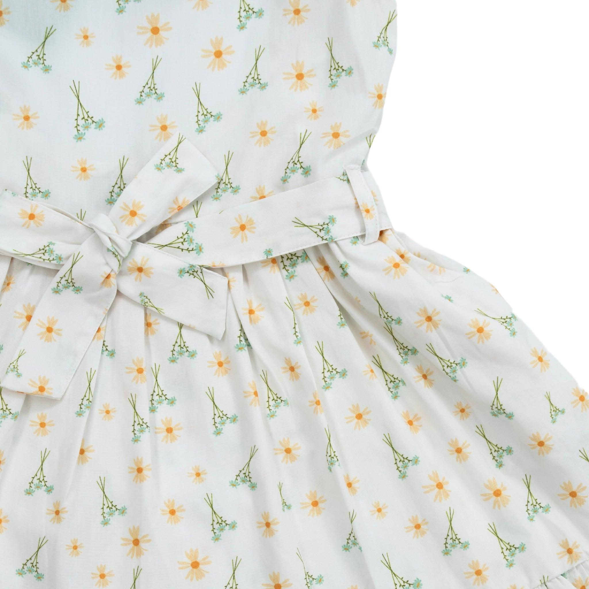 Close-up of a Karee Petite Blossom Cotton Dress in Smoked Pearl with a bow at the waist, featuring a pattern of yellow flowers and green sprigs on white fabric.
