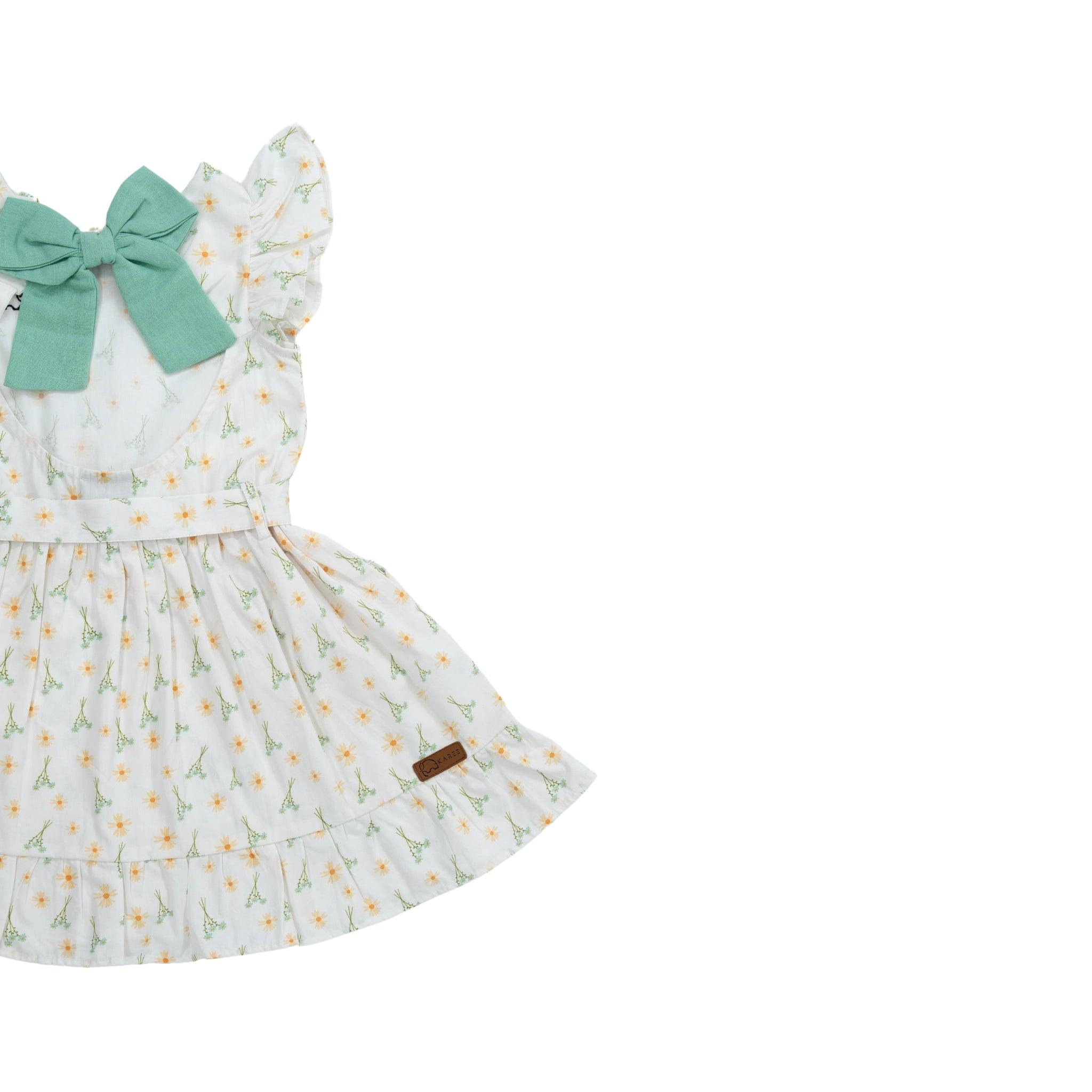 Karee Smoked Pearl Cotton Dress: White floral print toddler dress with a green bow, displayed on a clean, white background.