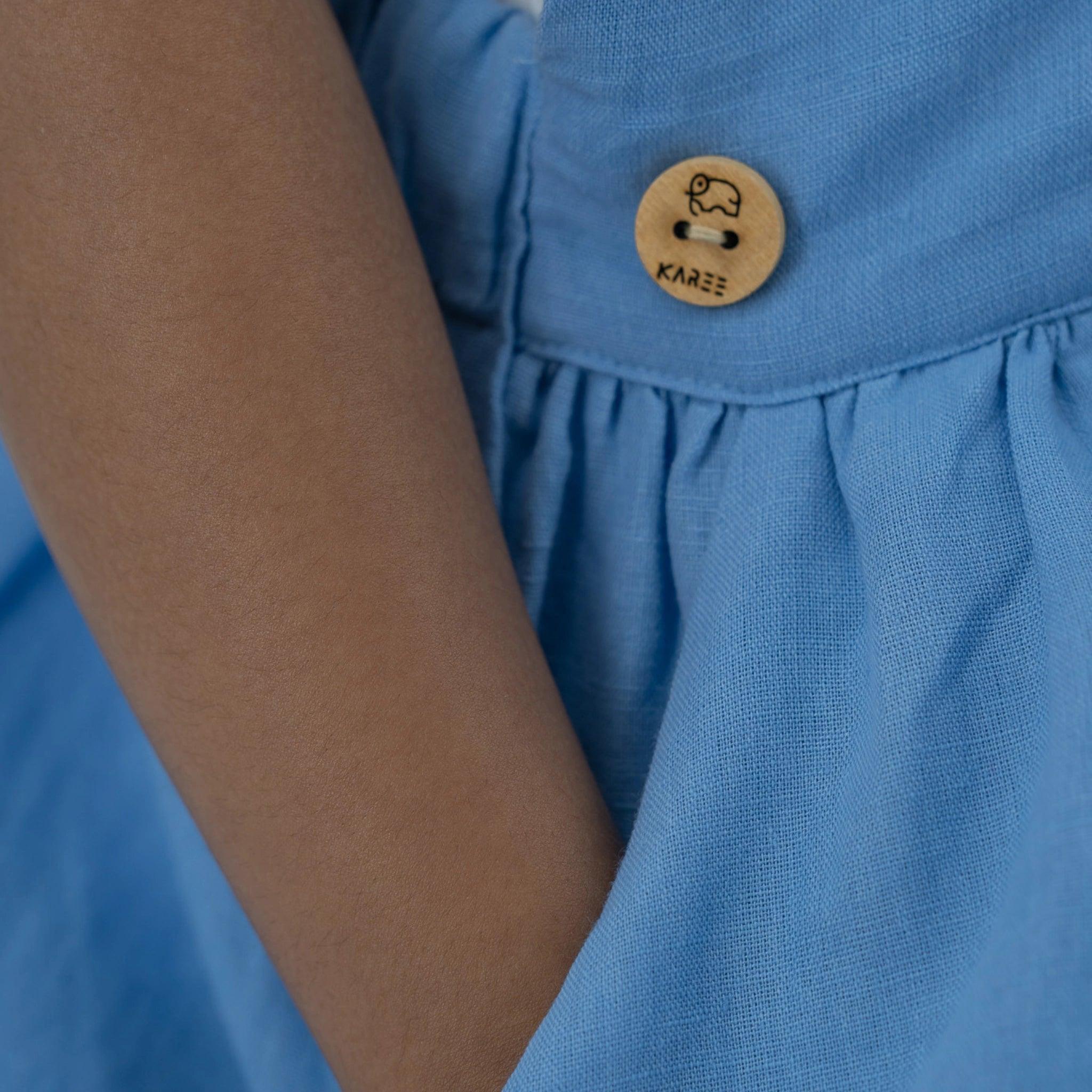 Close-up of a wooden button with an elephant design on a Karee Cerulean Blue Linen Pinafore.