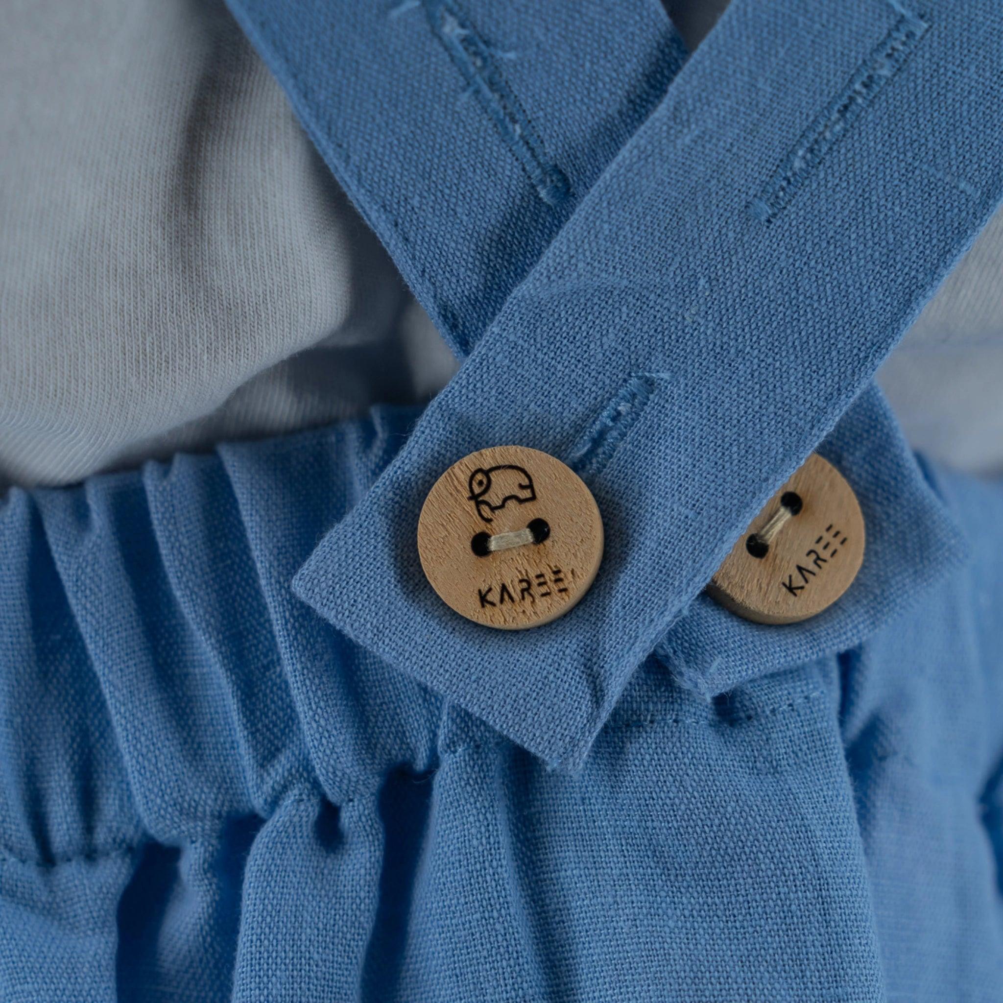 Close-up of a Karee Cerulean Blue Linen Pinafore with ruffled fabric and two wooden buttons.