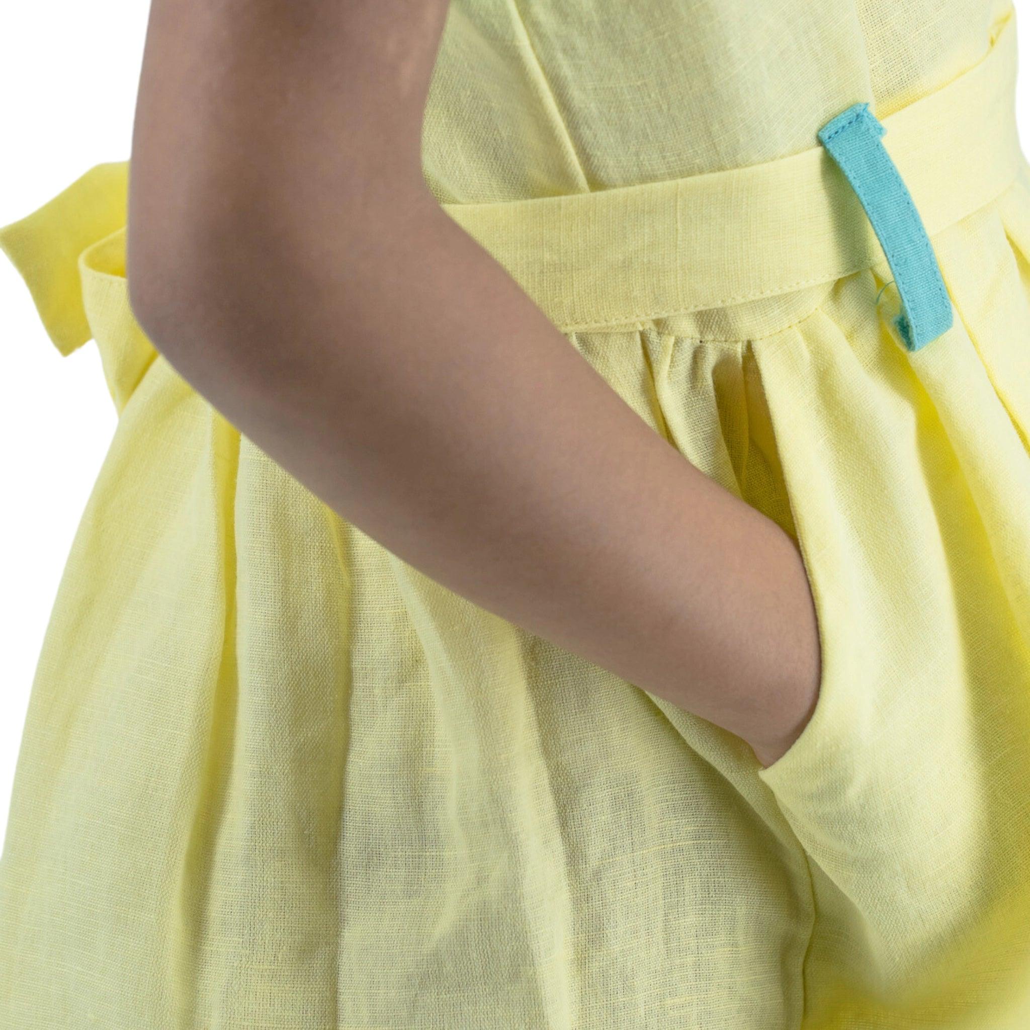 Close-up of a person in a Karee Elfin Yellow Linen Below Knee Length Dress for Girls with a blue belt loop detail, focusing on the waist area.