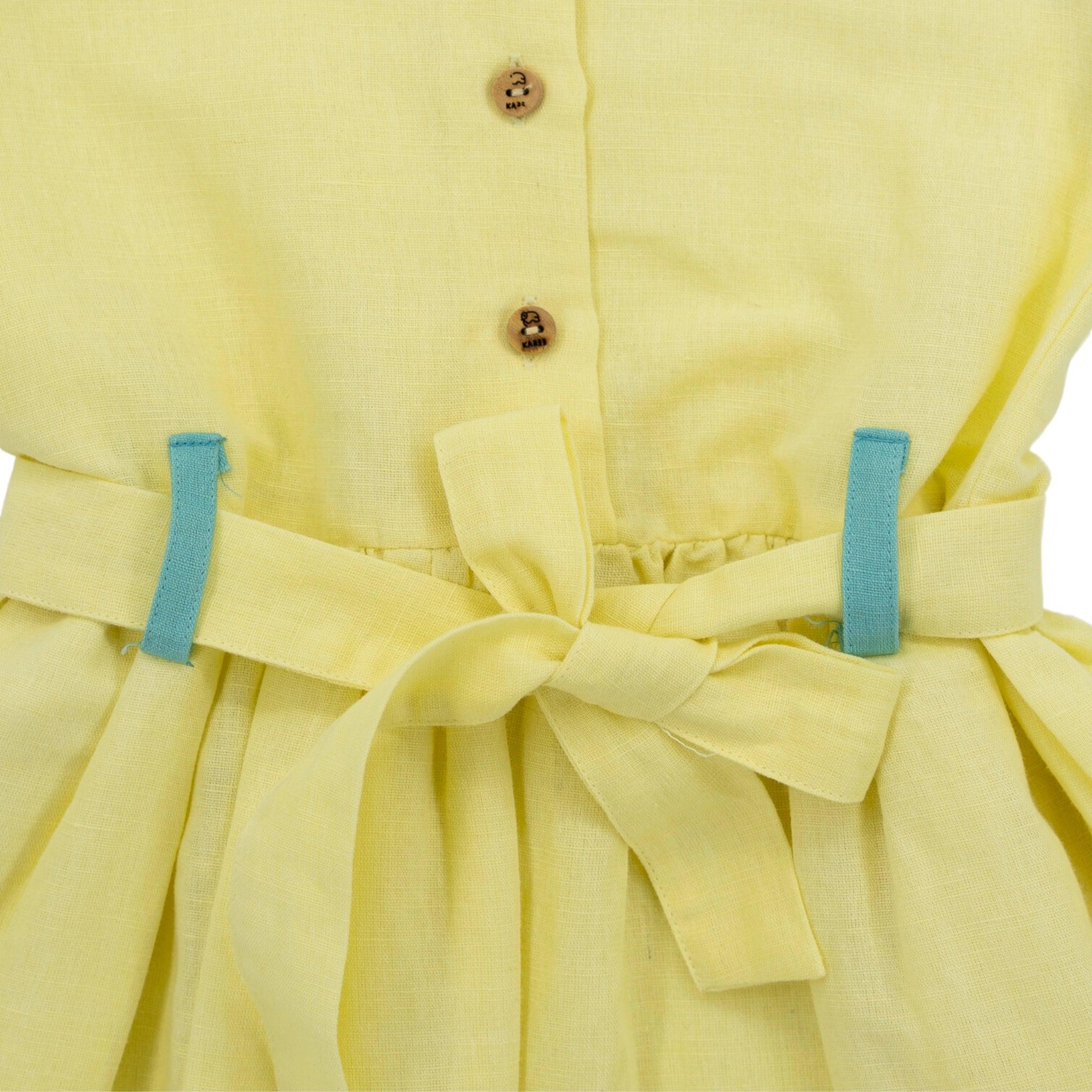 Close-up of a Karee Elfin Yellow Linen Below Knee Length Dress for Girls with a bow at the waist and two blue belt loops, focusing on texture and buttons.