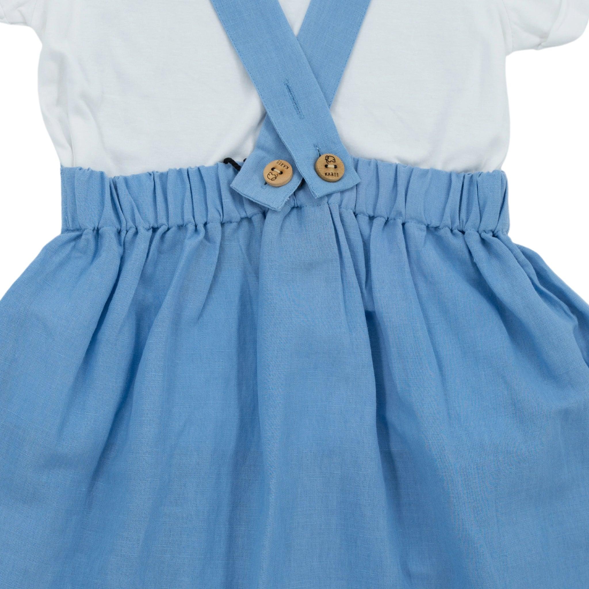 Close-up of a child's outfit featuring a white shirt and a Karee cerulean blue linen pinafore with suspenders and button details.