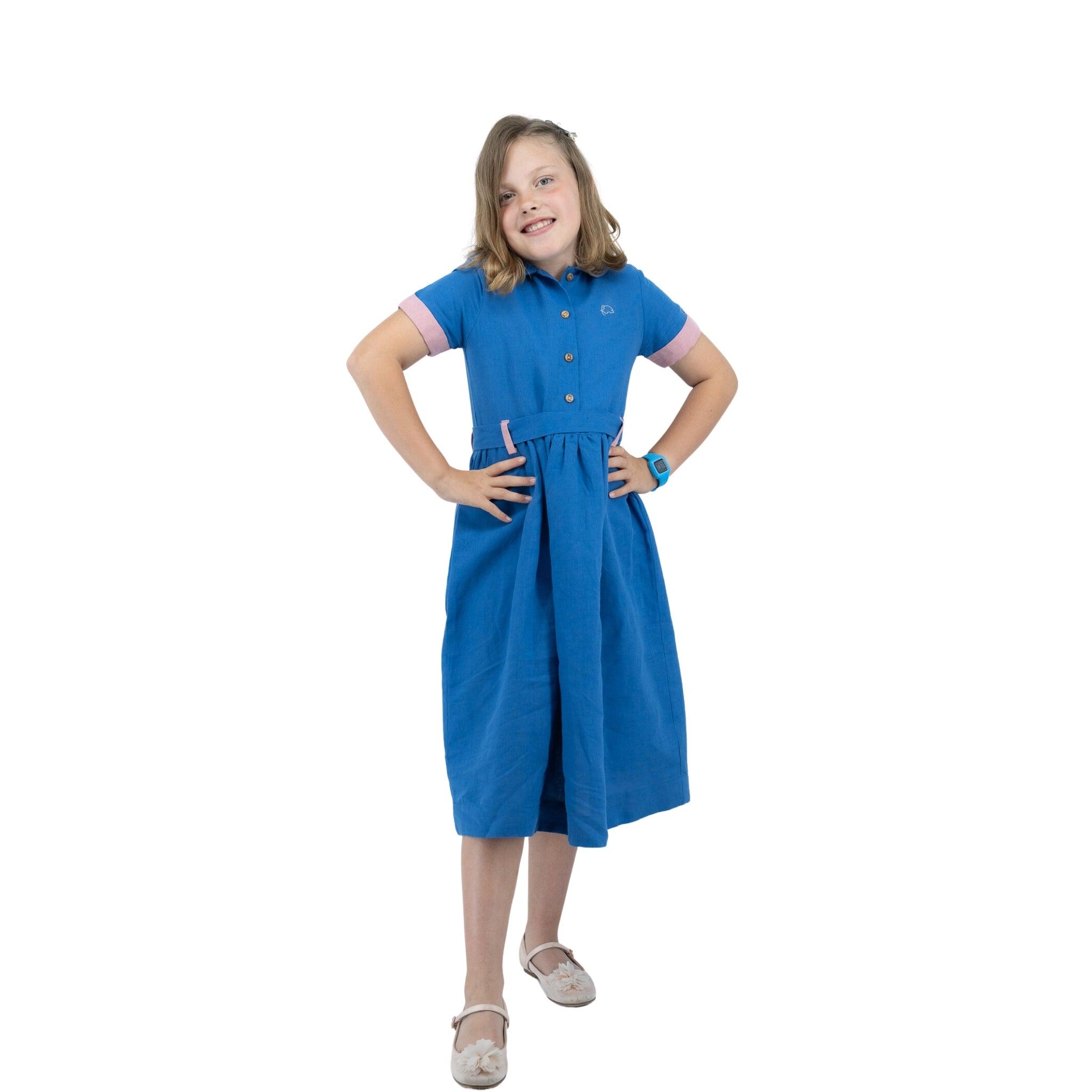 Young girl in a Karee Parisian Blue Linen Dress for Girls standing with hands on hips and smiling, isolated on white background.