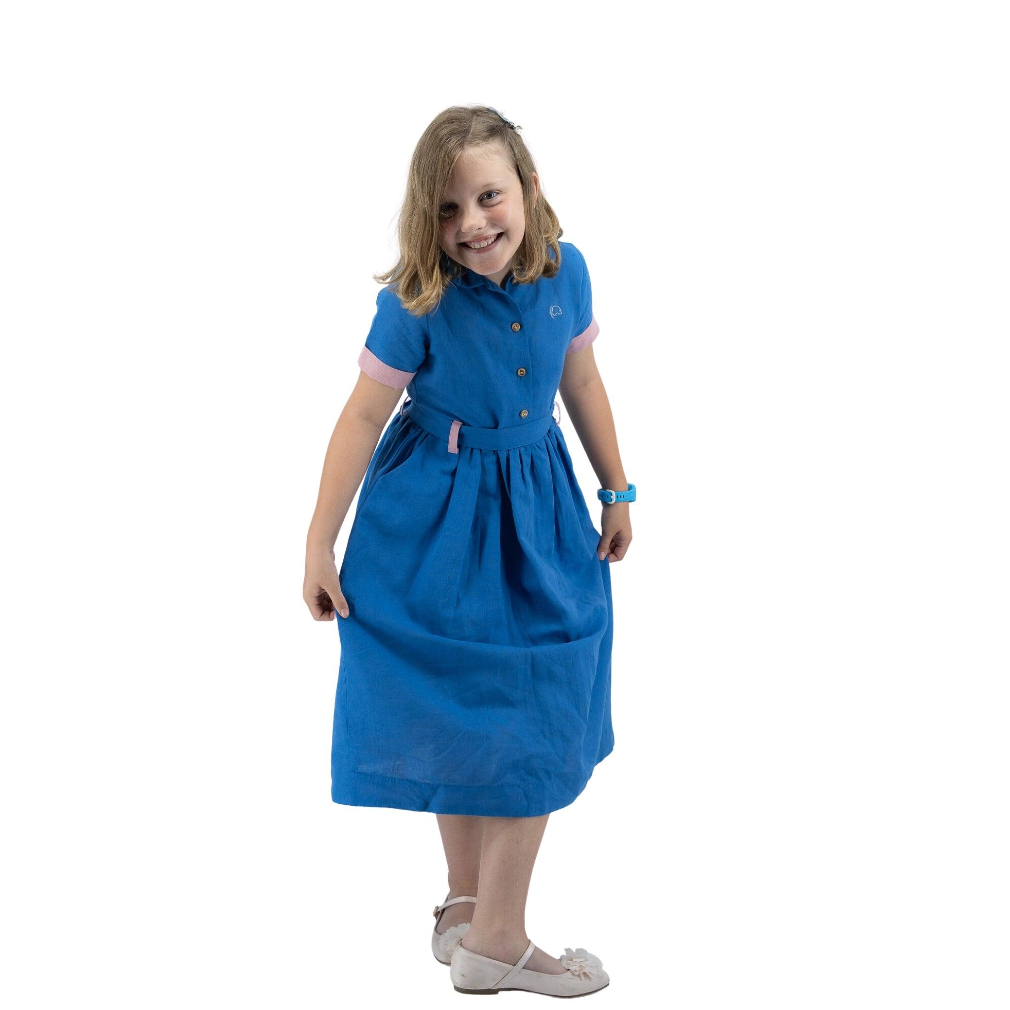Young girl in a Karee Parisian Blue Linen Dress for Girls smiling and posing, standing against a white background.