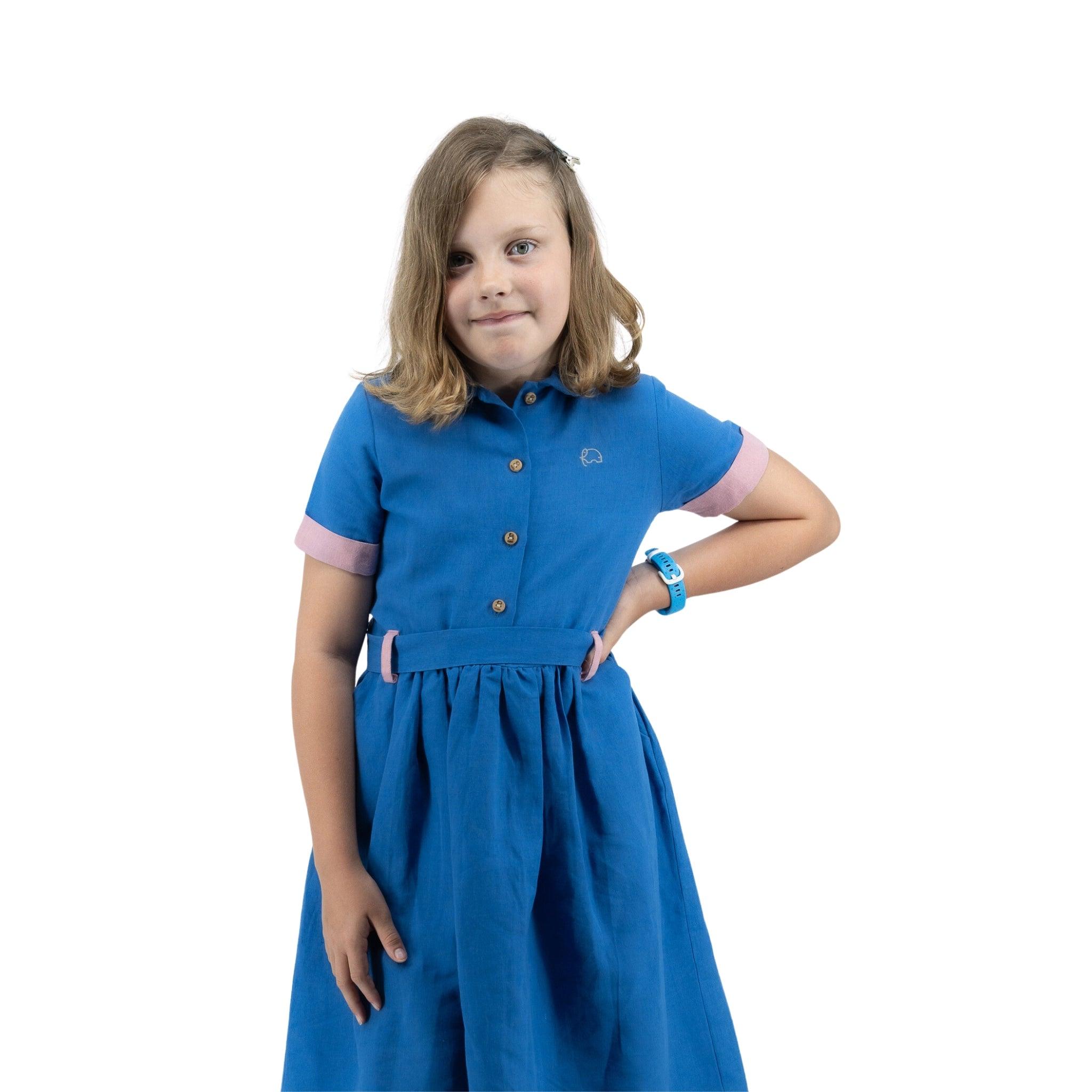 Young girl in a Karee Parisian Blue Linen Dress for Girls with hands on hips, smiling slightly, standing against a white background.