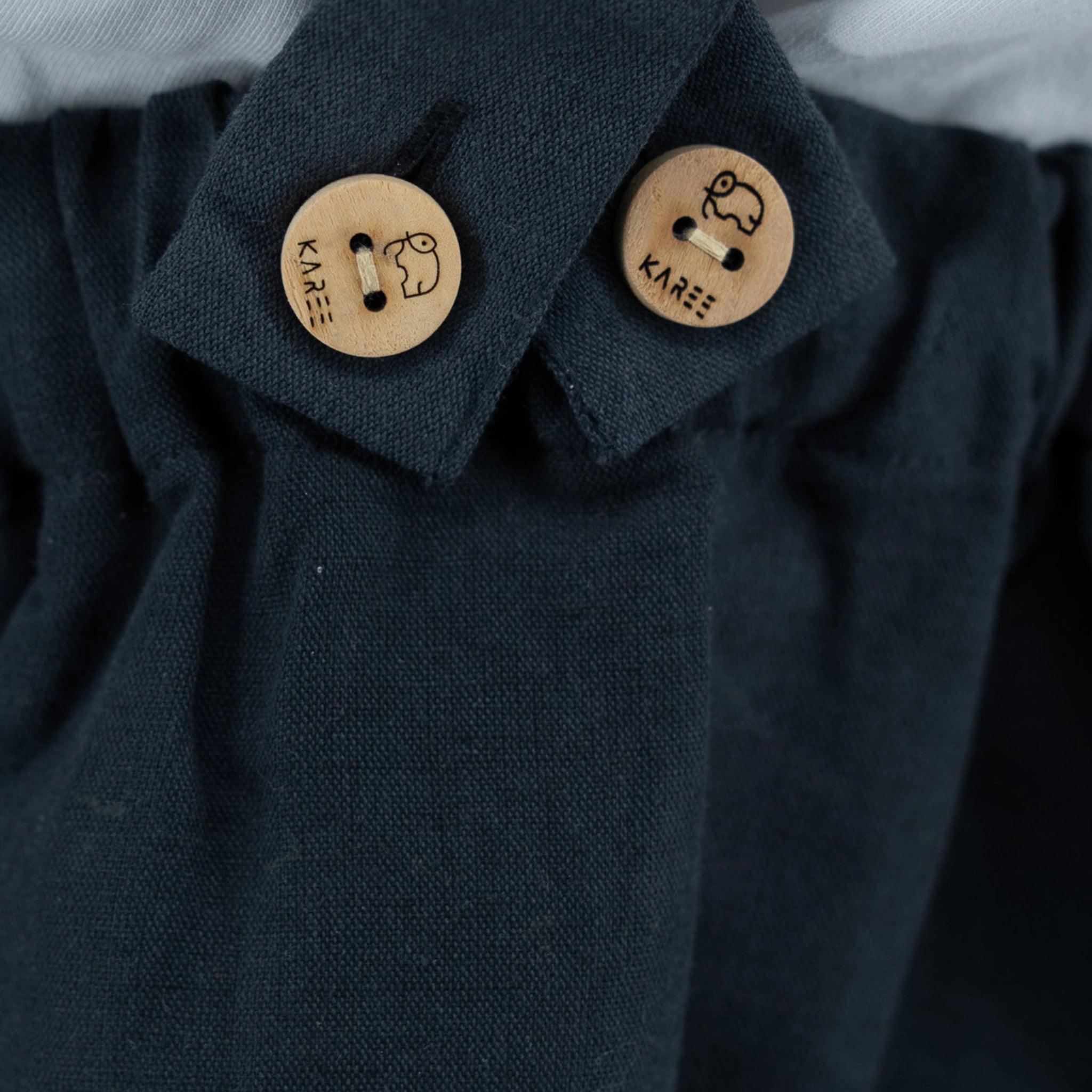 Close-up of a Karee ebony black linen pinafore for girls with two wooden buttons engraved with a key design and the text "kaze", embodying timeless sophistication.
