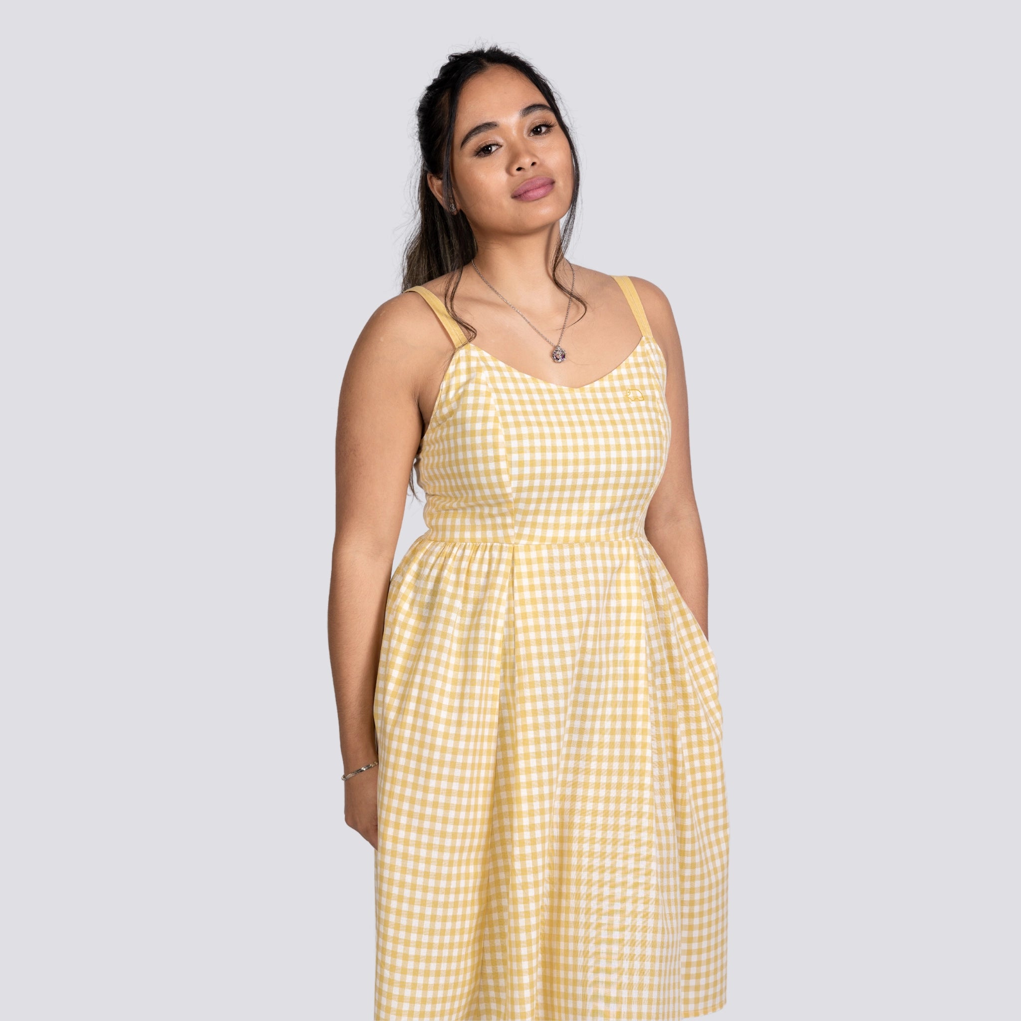 Woman standing against a gray background, wearing a Karee Sunshine Chic Yellow Plaid Cotton Mini Dress and a pendant necklace, looking slightly to the side.