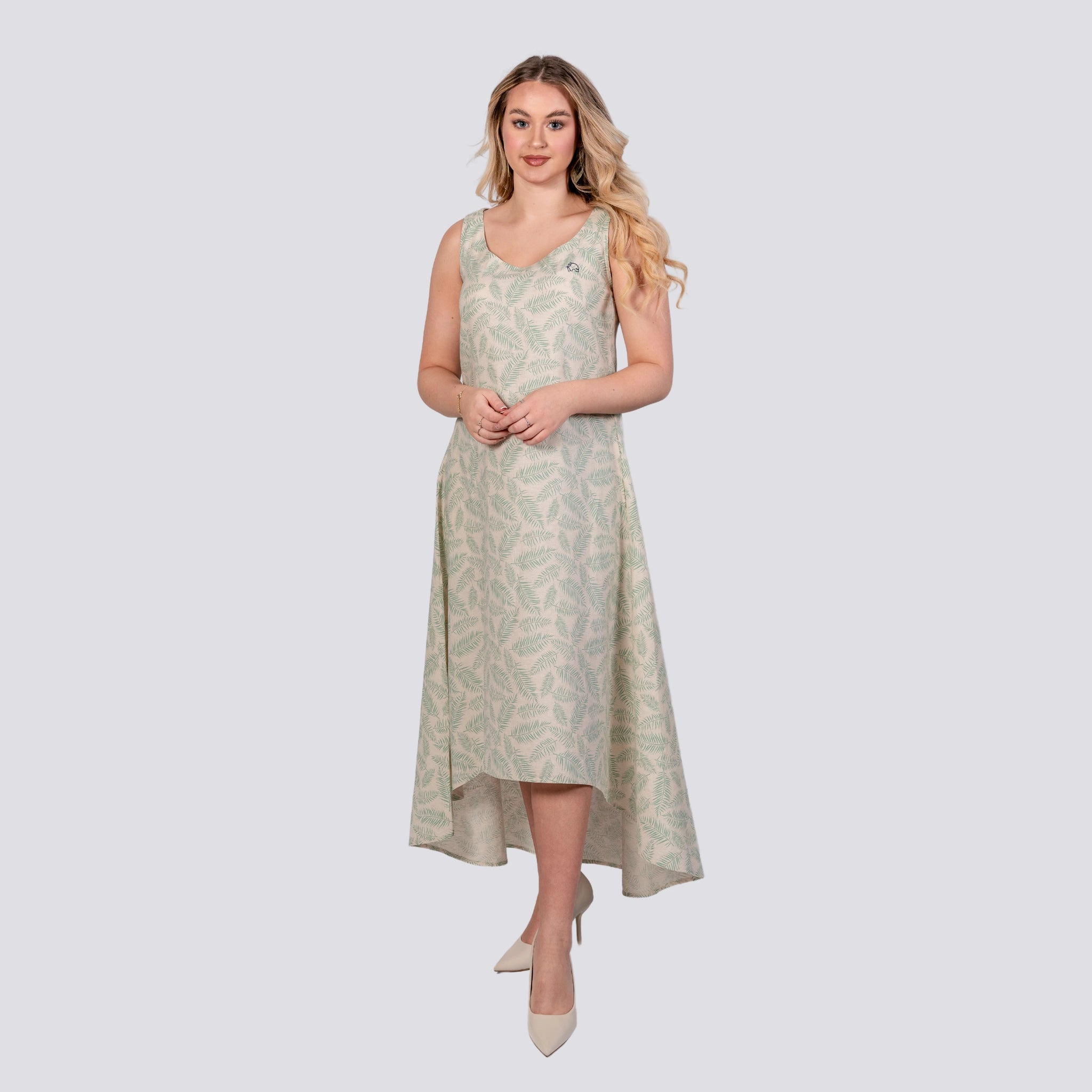 A woman in a Karee Mystic Breeze High Low Linen Cotton Midi Dress stands confidently, her hands clasped in front, wearing white heels against a light gray background.