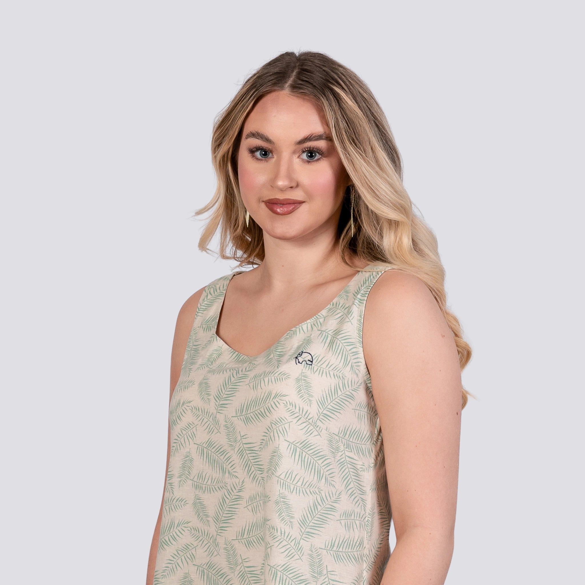 A young woman with blonde hair smiling at the camera, wearing a sleeveless U-neck top with a fern pattern. The background is light gray.
Product: Karee Mystic Breeze High Low Linen Cotton Midi Dress