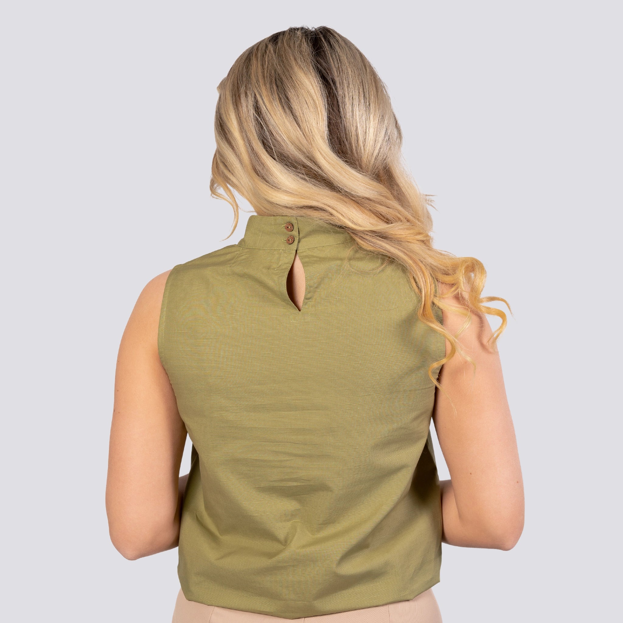 Woman with blonde hair viewed from behind, wearing a sleeveless Karee Pear Green Harmony Sleeveless Top For Women made of eco-friendly linen and cotton, featuring a buttoned keyhole neckline.