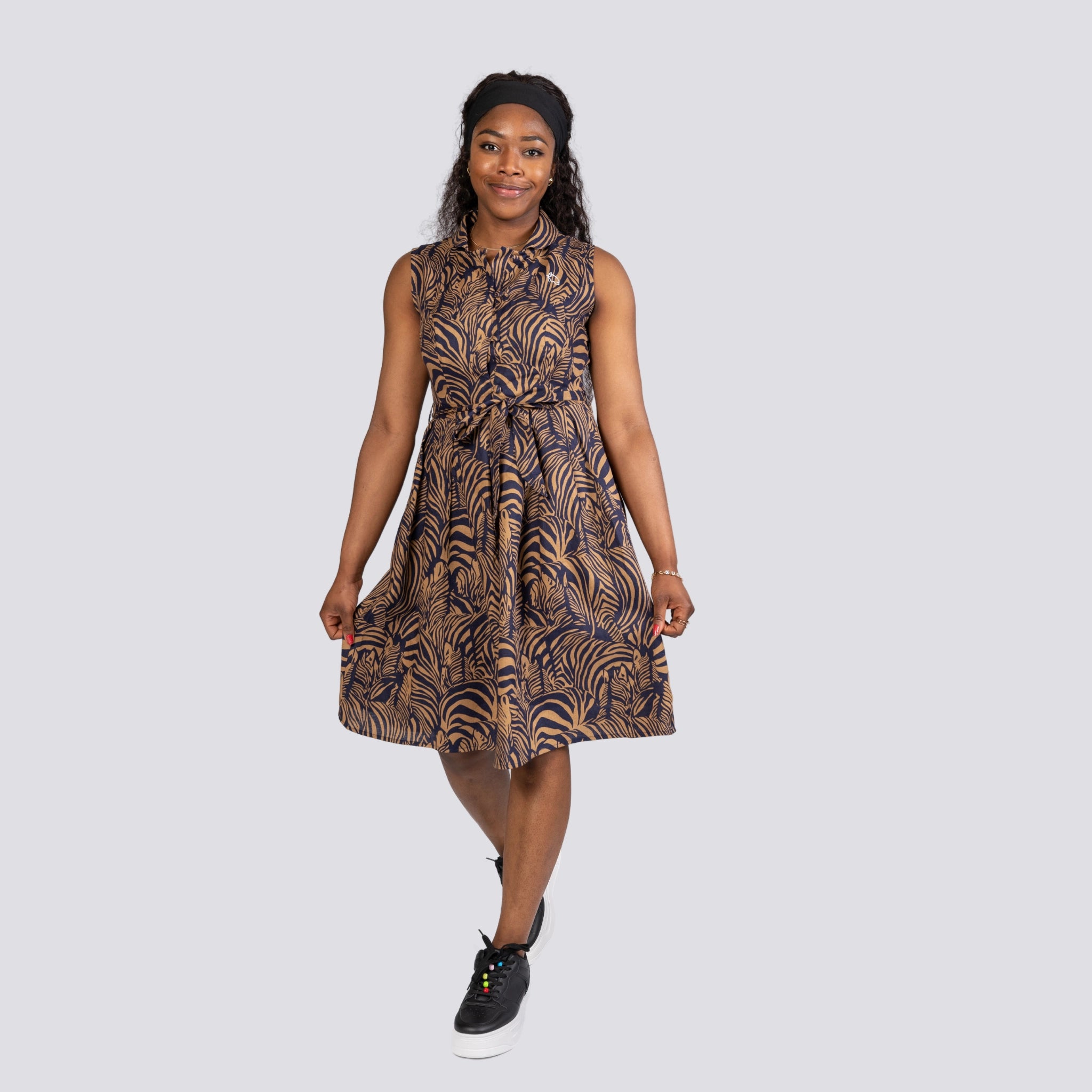 A woman in a navy blue patterned Linen Enchantment Button-Up Midi Dress by Karee, smiling and standing against a light grey background, wearing sneakers.