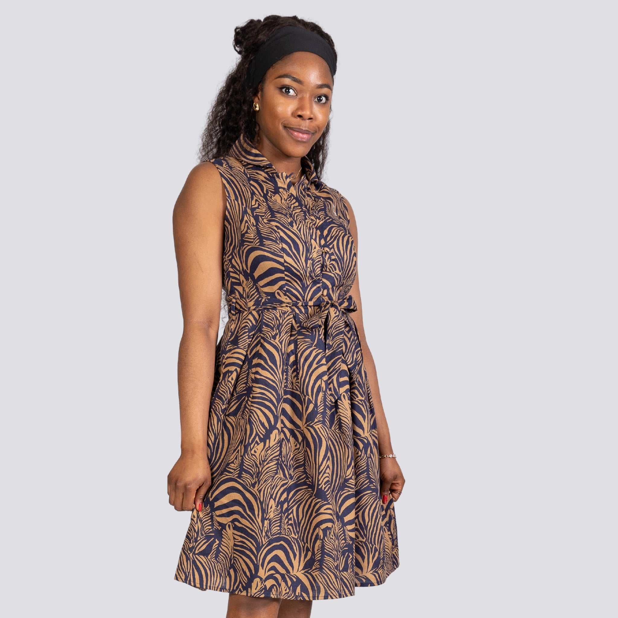 A young woman in a sleeveless navy blue patterned dress stands confidently, looking to the side, isolated on a light gray background. (Product: Linen Enchantment Button-Up Midi Dress, Brand: Karee)