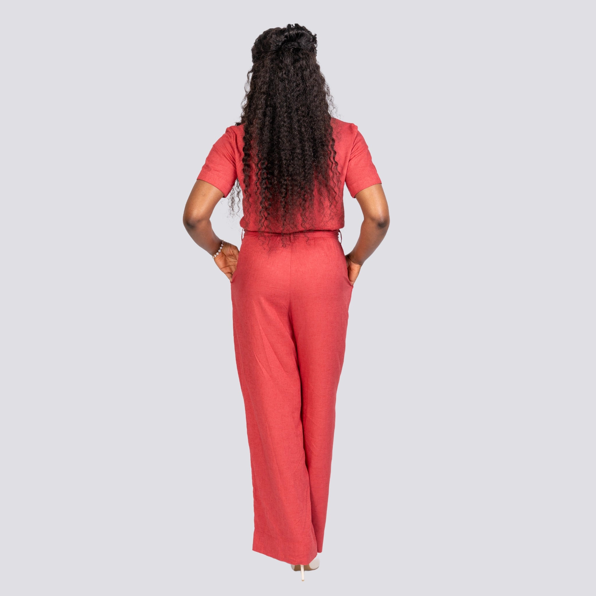 Woman in Karee Milano Red Serenity Viscose Linen Jumpsuit standing with her back to the camera, hands on hips, against a light gray background.