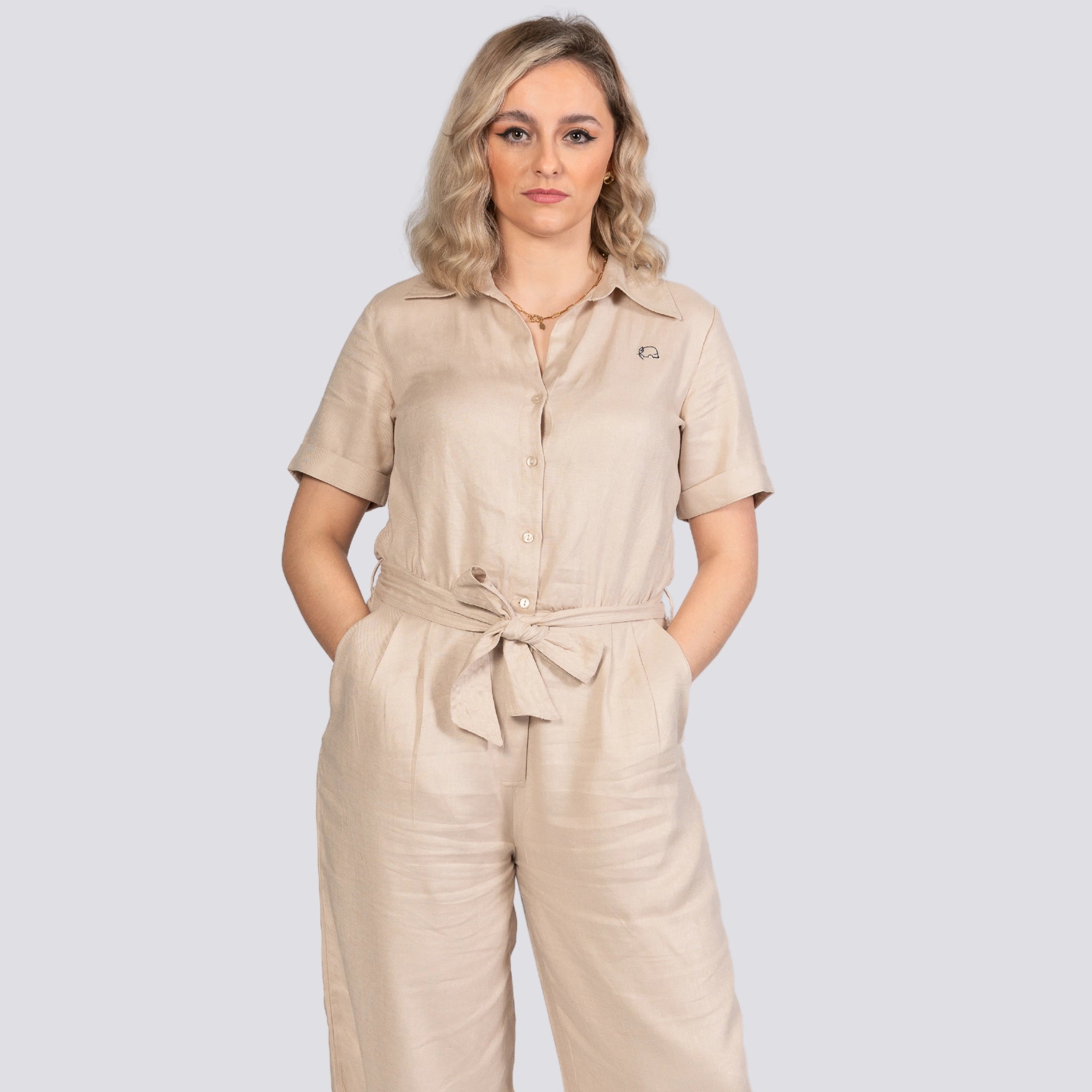 Woman standing against a grey background, wearing a Karee Merino Elegance Viscose Linen Jumpsuit with a tie waist, looking at the camera.