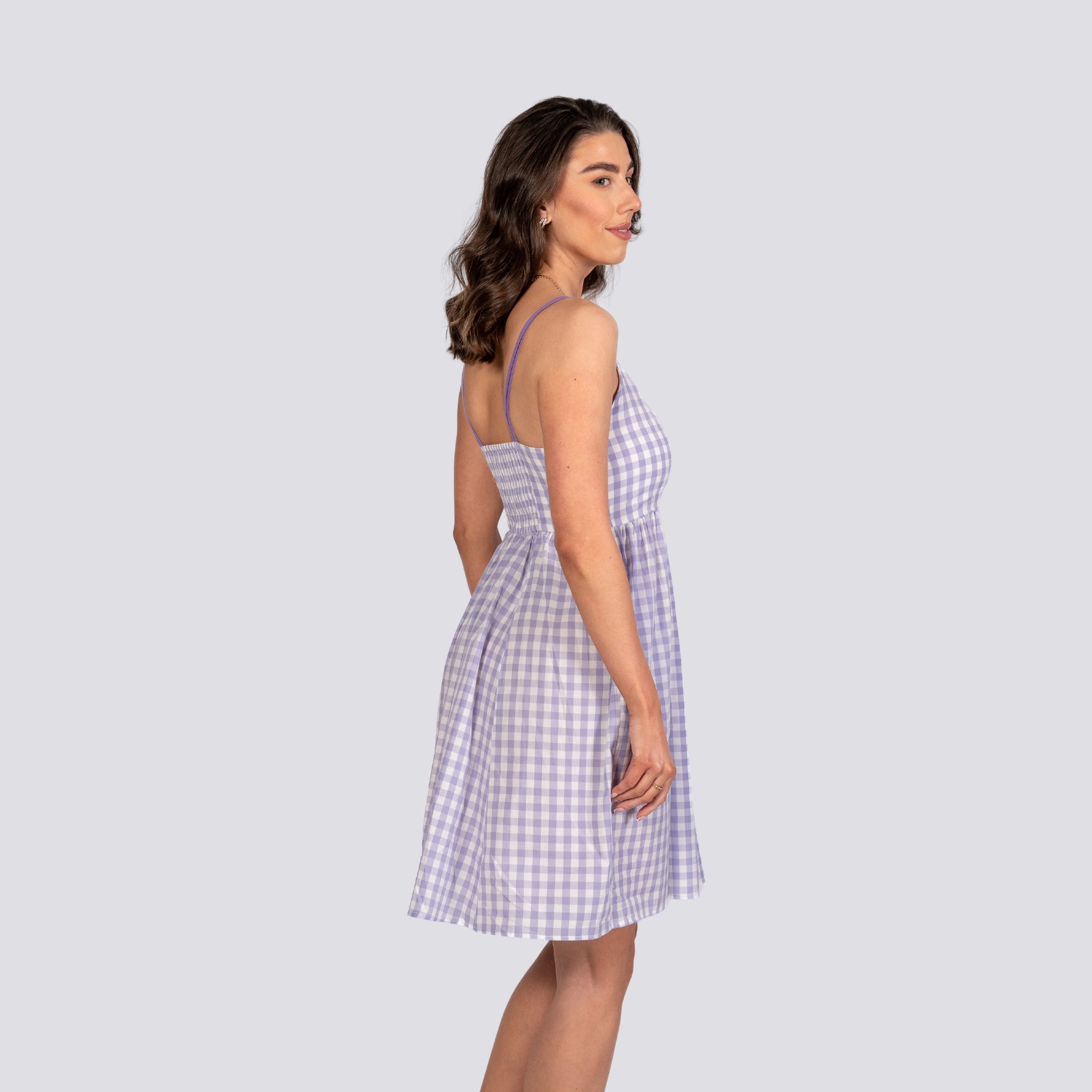 Woman in a Karee Lavender Plaid Cotton Mini Dress looking over her shoulder, standing against a light gray background.
