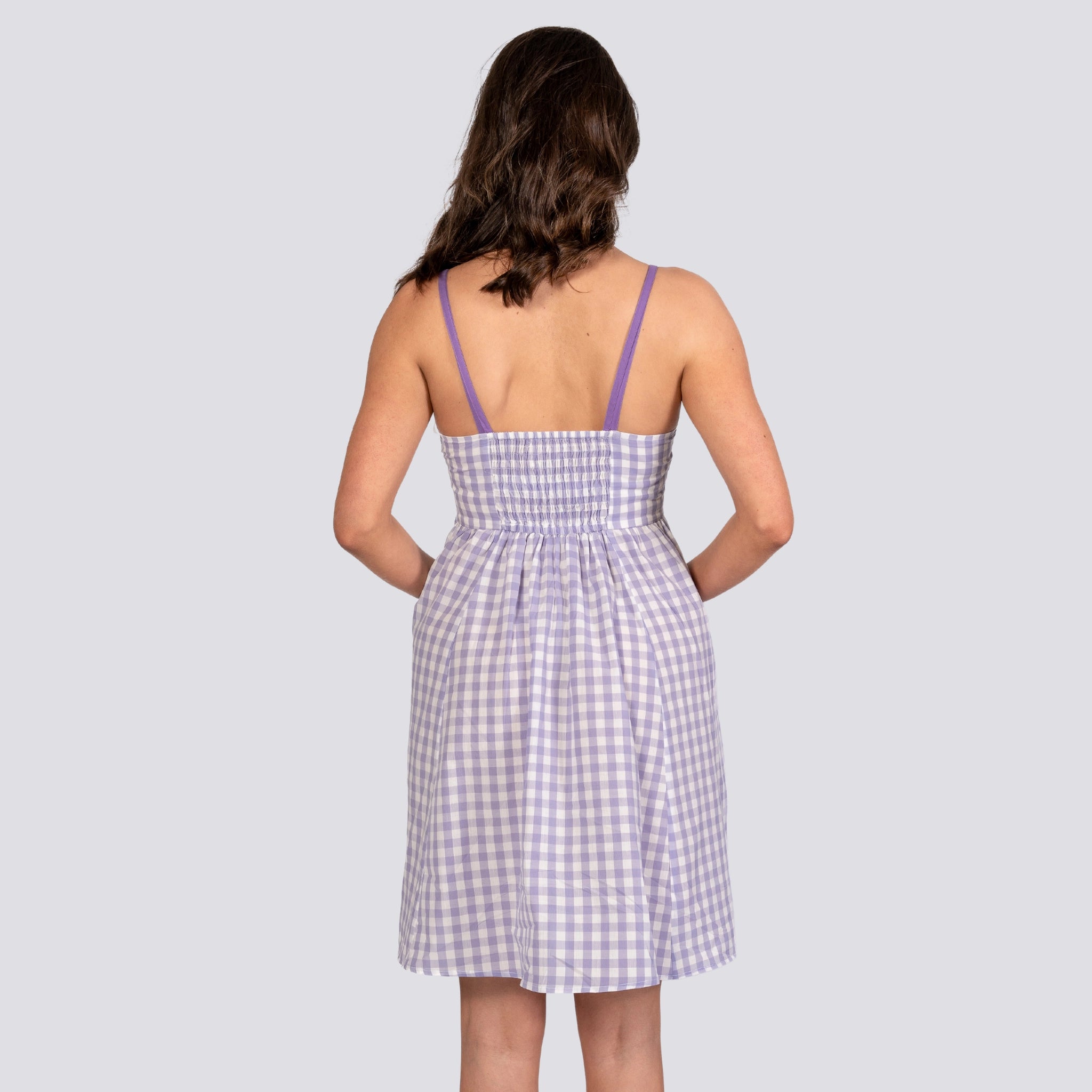 A woman seen from behind, wearing a Karee Lavender Plaid Cotton Mini Dress For Women with thin straps, standing against a gray background.