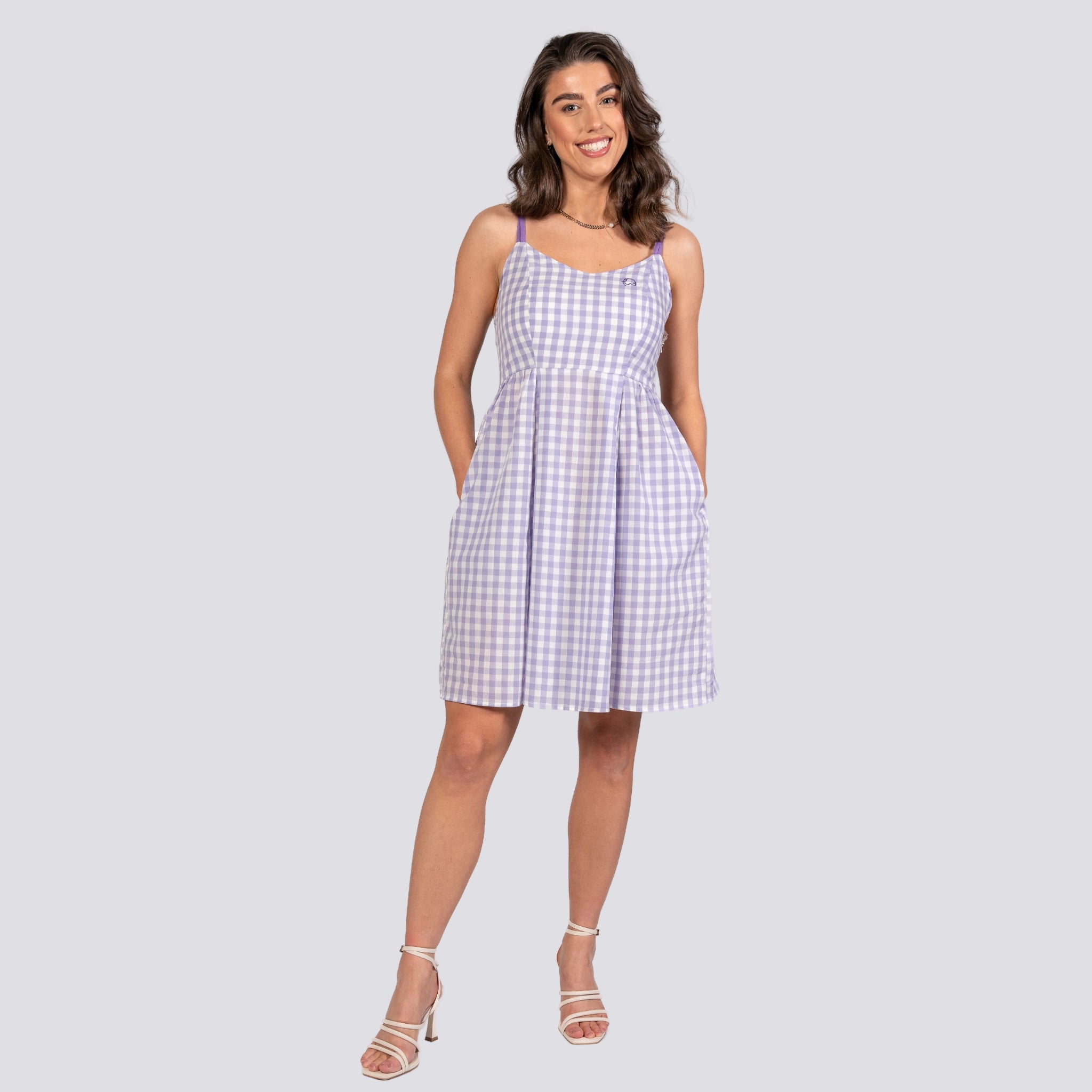 A woman in a Karee Lavender Plaid Cotton Mini Dress and white heels smiles while posing against a plain background.