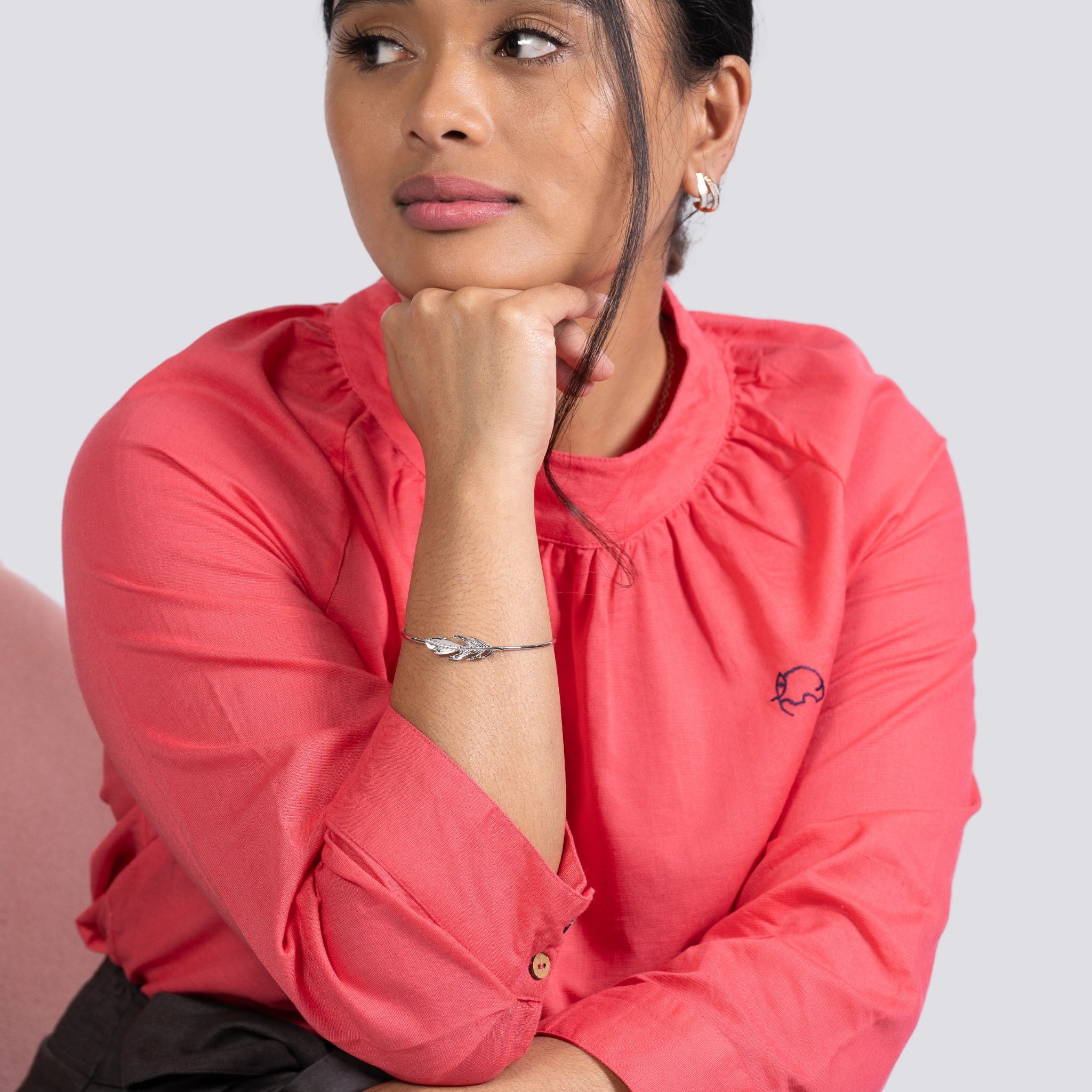 Woman in a Karee fuchsia elegance high neck top and a silver bracelet, resting chin on hand, looking thoughtful. Light gray background.