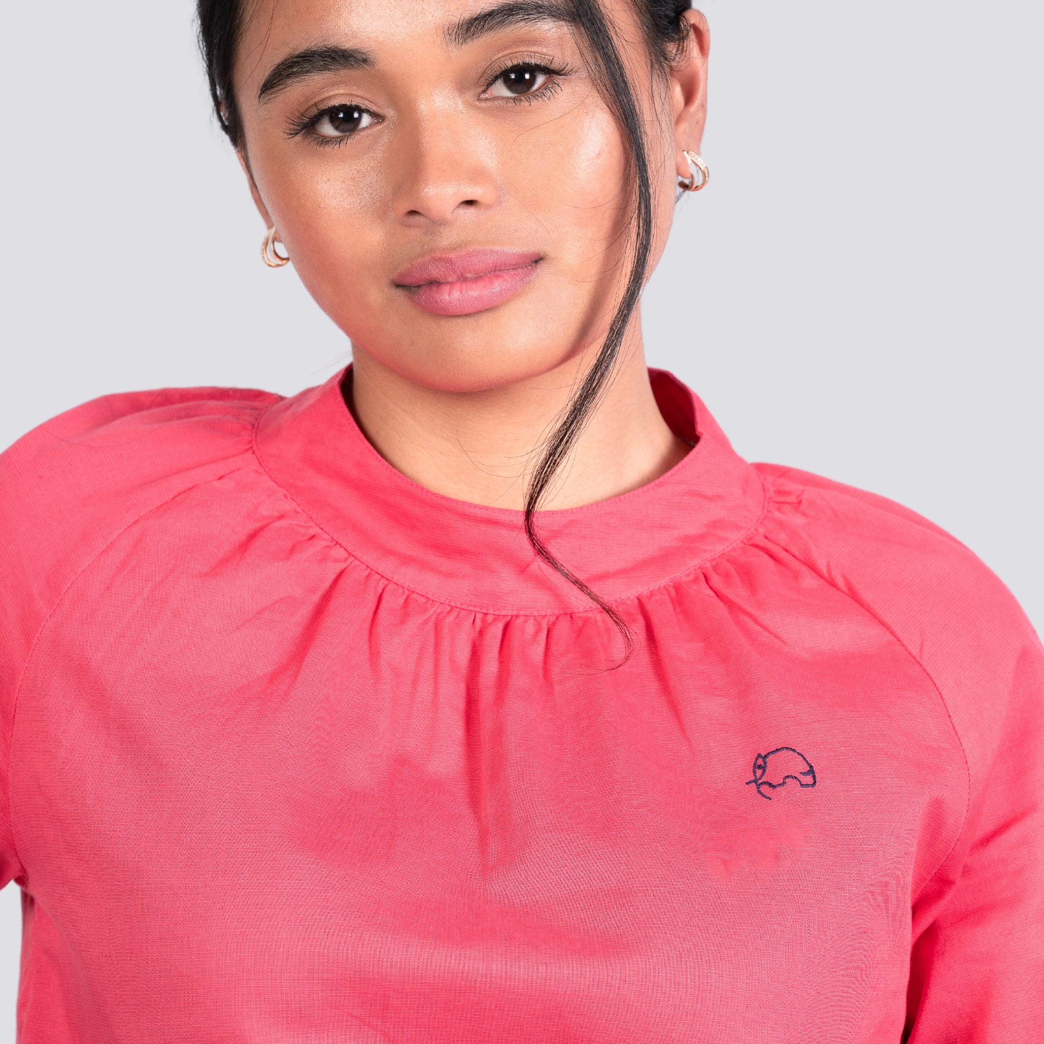 Woman in a Karee Fuchsia Elegance High Neck Top, looking at the camera, light makeup, with a loose strand of hair across her face.