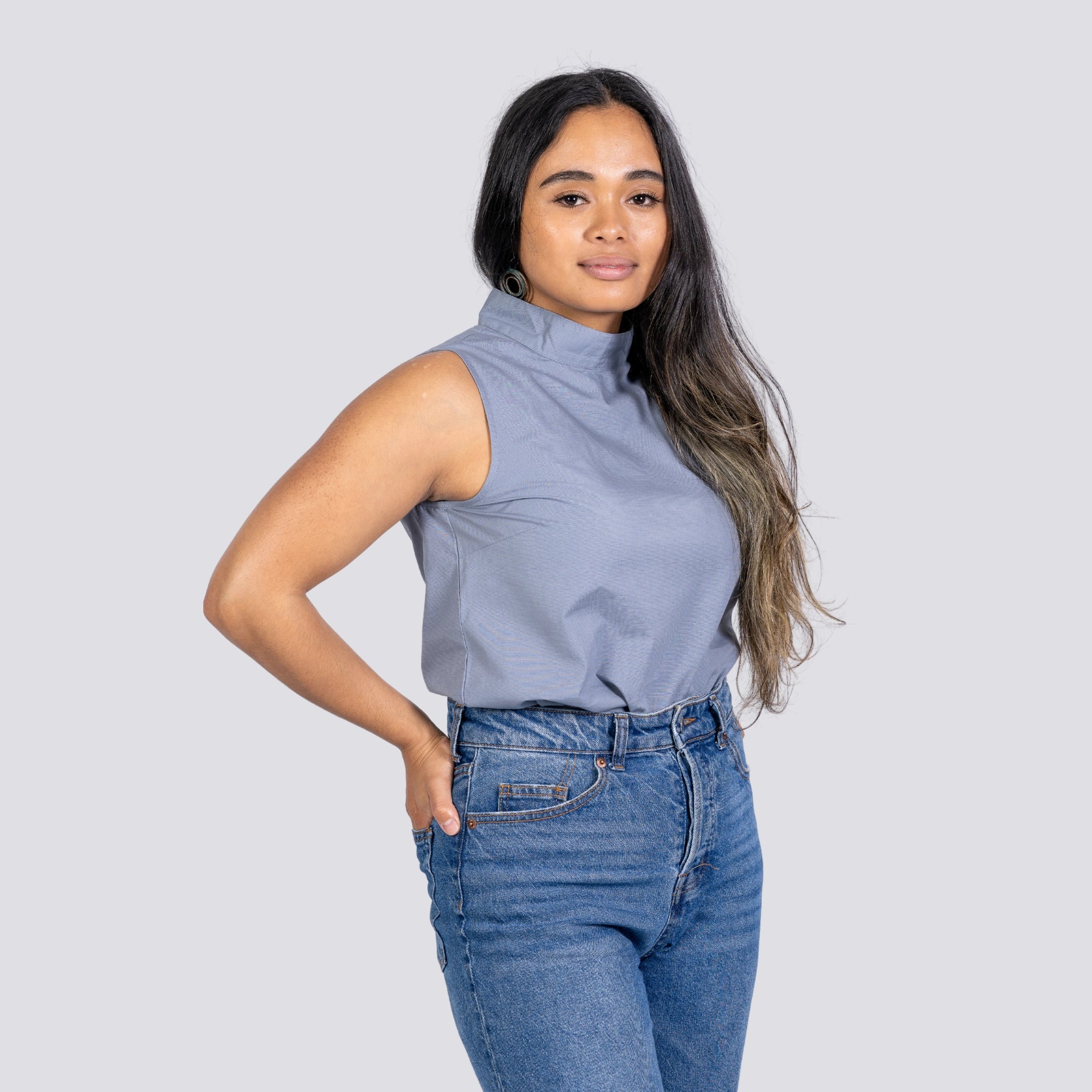 Woman in a Karee Linen Sleeveless Top in Classic Grey and jeans posing with her hand on her hip against a gray background.