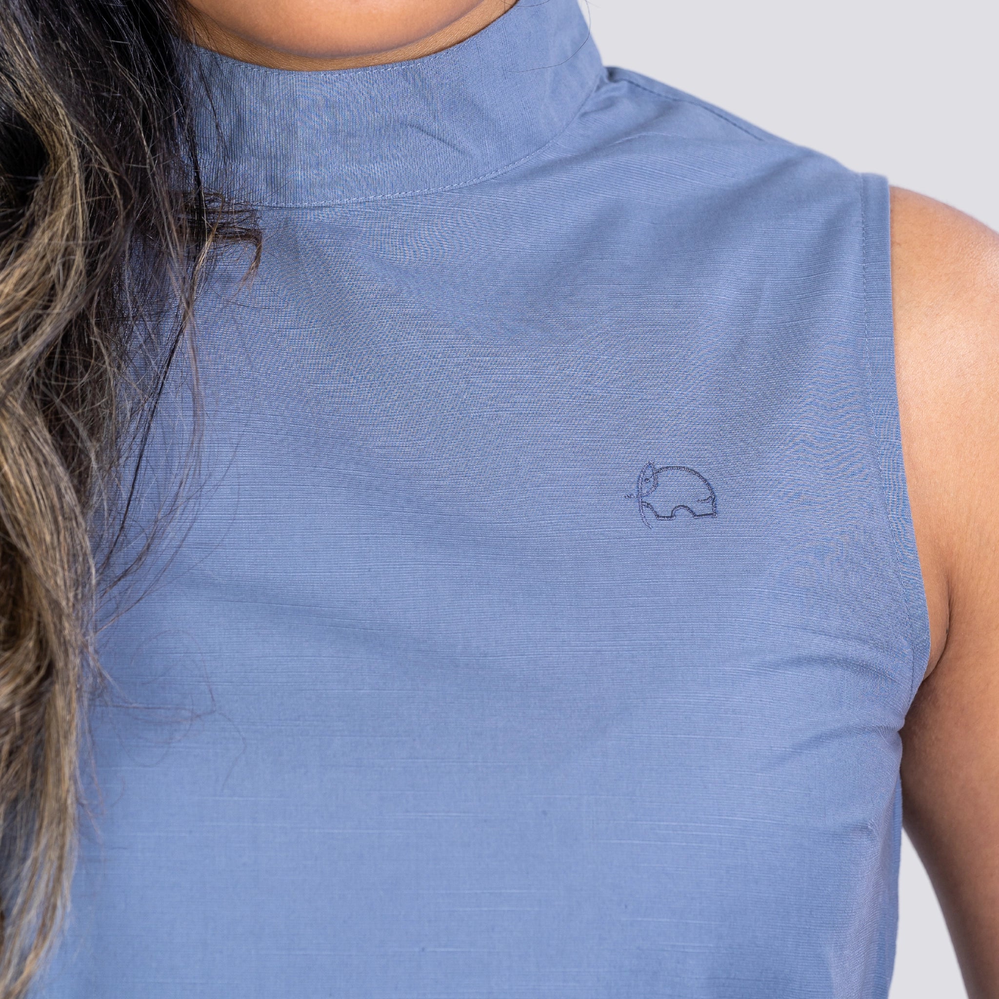 Close-up of a woman wearing a Karee Linen Sleeveless Top in Classic Grey featuring a small elephant logo embroidered near the shoulder.