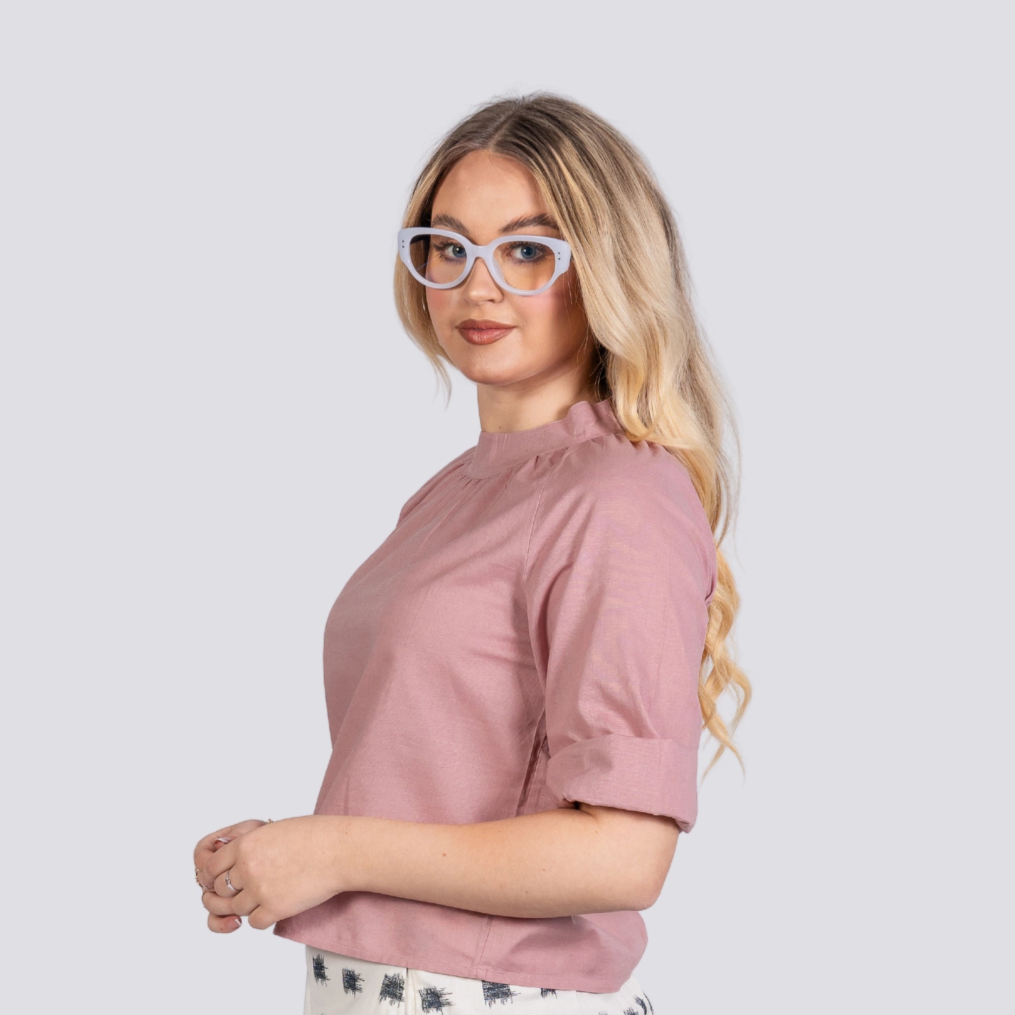 Young woman wearing glasses and a Karee Flamingo Rose 3/4 Sleeve Linen-Cotton Top For Women, standing confidently with her hands clasped, against a plain background.