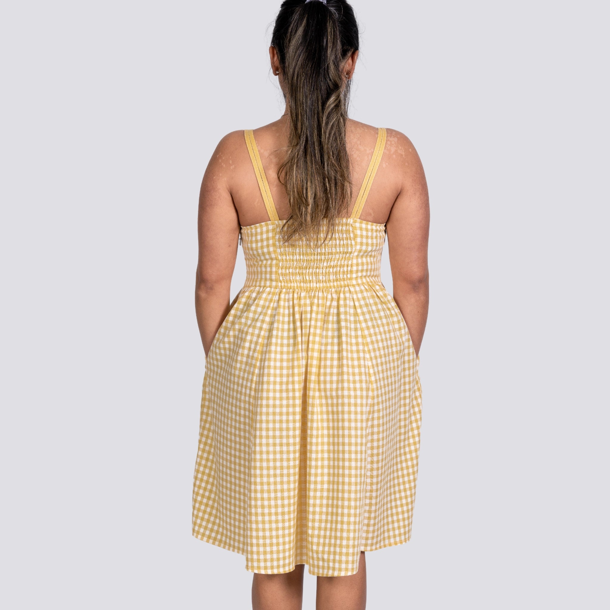 Woman viewed from behind, wearing a Karee Sunshine Chic Yellow Plaid Cotton Mini Dress with thin straps, standing against a gray background.
