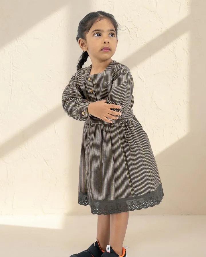 Girls' autumn dress: a girl in the Black stripe long puff-sleeve cotton dress with a broderie anglaise hem, arms folded