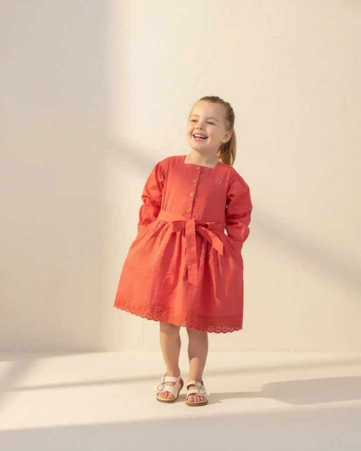 Girls' autumn dress: a smiling girl in the Coral long puff-sleeve cotton dress with a tie belt and broderie anglaise hem